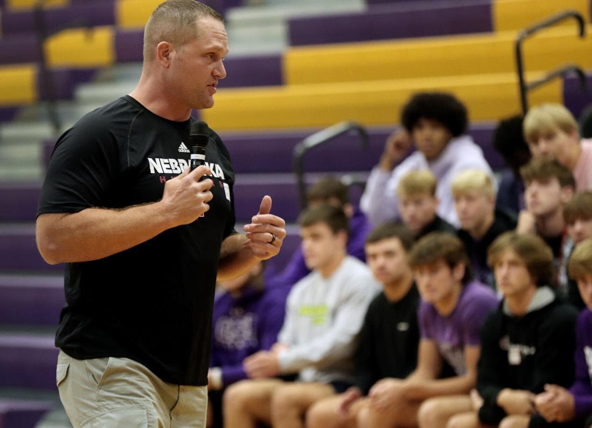 Adam Carriker speaking with a microphone to a high school team seated in a gymnasium
